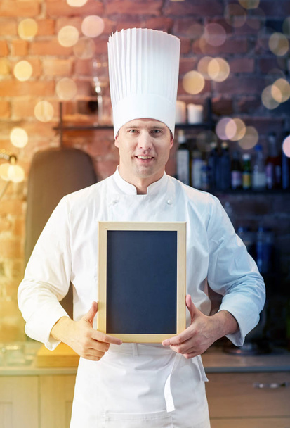 happy male chef with blank menu board in kitchen - Foto, afbeelding