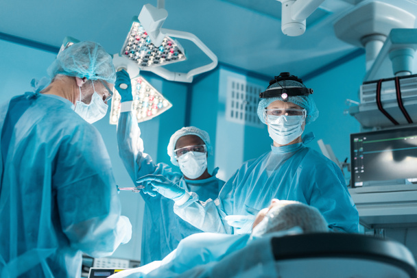 мультикультурные хирурги и пациенты во время операции в операционной
 - Фото, изображение