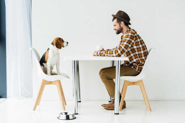 Widok z boku mężczyzny i ładny pies gończy, siedząc przy stole - Zdjęcie, obraz