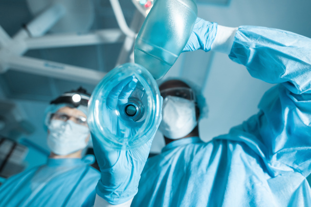 Blick von unten auf den afrikanischen Anästhesisten mit Sauerstoffmaske über dem Patienten - Foto, Bild