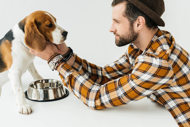 side view of man palming dog at table with pet bowl - Photo, Image