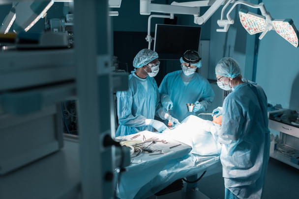 tres cirujanos multiculturales y paciente en quirófano
 - Foto, imagen