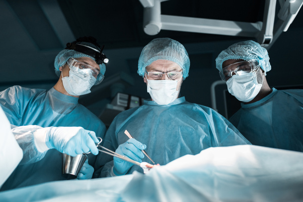 multicultural surgeons operating patient in operating room - Photo, Image