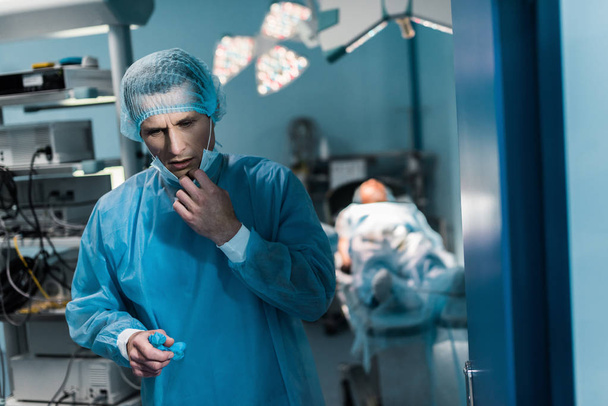 усталый врач снимает медицинскую маску в операционной
 - Фото, изображение