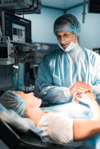 χαμογελώντας γιατρού και ασθενούς, κρατώντας τα χέρια στο χειρουργείο - Φωτογραφία, εικόνα