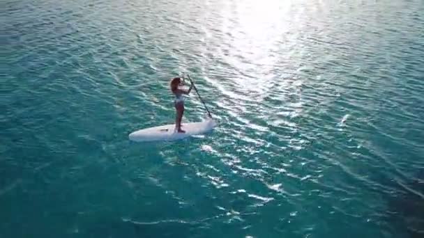 Vista aérea de chica joven de pie remando en vacaciones. Tracking shot of a young woman SUP boarding
 - Metraje, vídeo