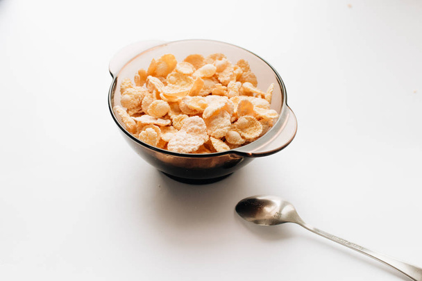 heerlijke krokante cornflakes in kom met lepel op witte achtergrond, gezond ontbijt - Foto, afbeelding