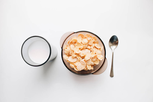 ποτήρι γάλα και νόστιμα τραγανά δημητριακά στο μπολ με το κουτάλι σε άσπρο φόντο, υγιεινό πρωινό - Φωτογραφία, εικόνα