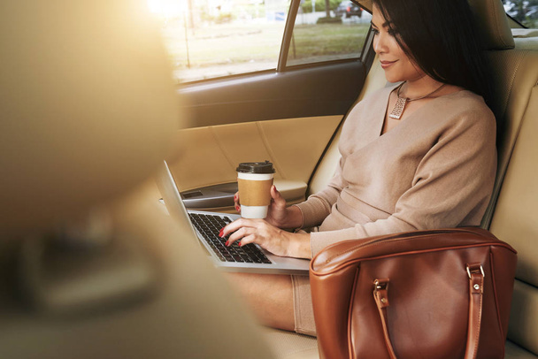 Mosolygó üzleti hölgy kávét iszik, és működő-ra laptop - Fotó, kép