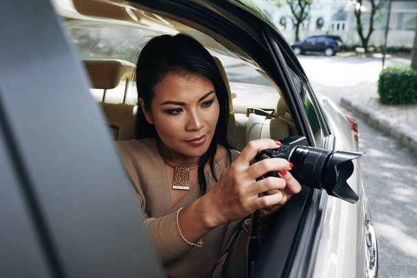 Atraktivní mladá žena sedí v autě a pořizování fotografií na digitální fotoaparát - Fotografie, Obrázek