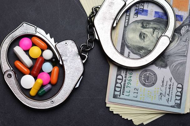 Menottes, drogues et billets de banque en dollars sur fond sombre suggérant une punition pour trafic illicite de substances
  - Photo, image