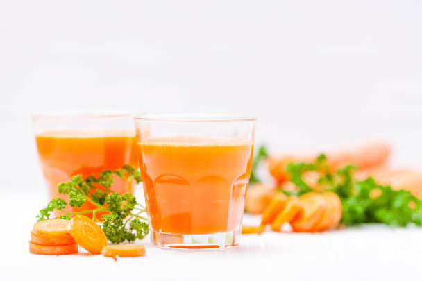 Succo di carota in bei bicchieri, verdure arancioni tagliate e prezzemolo verde su sfondo di legno bianco. Una bevanda all'arancia fresca. Chiudi la fotografia. Concentrazione selettiva. Bandiera orizzontale
 - Foto, immagini