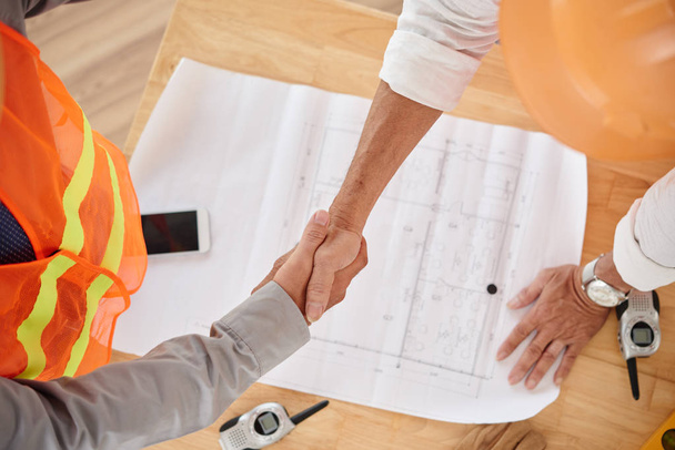 Firm handshake of contractor and head engineer, table with blueprint - Photo, Image