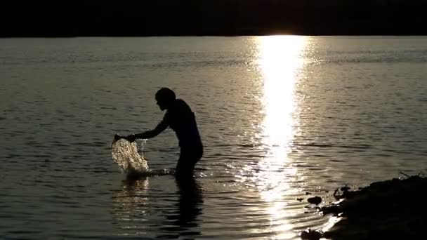 Mladý muž vytáhne šampion misku z jezera při západu slunce v slo-mo - Záběry, video
