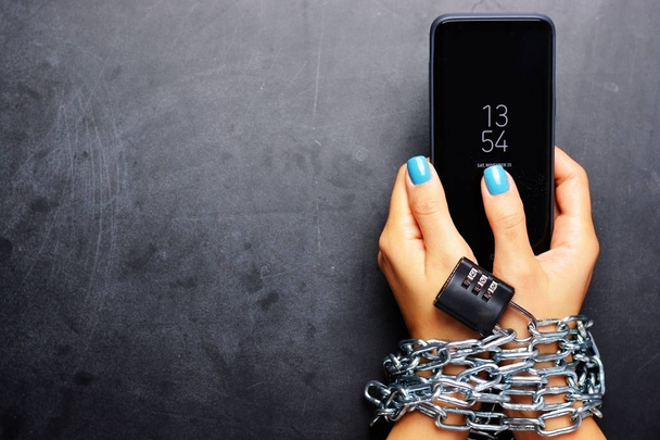 Руки женщины связаны металлической цепью с замком на темном фоне, что предполагает интернет или зависимость от социальных сетей
 - Фото, изображение