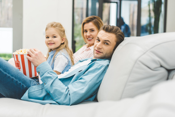 Zijaanzicht van de familie met popcorn camera kijken terwijl het letten van film samen thuis - Foto, afbeelding
