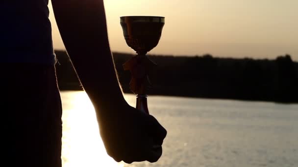 Man s hand houdt een kom van de winnaar aan de oever van een meer bij zonsondergang - Video
