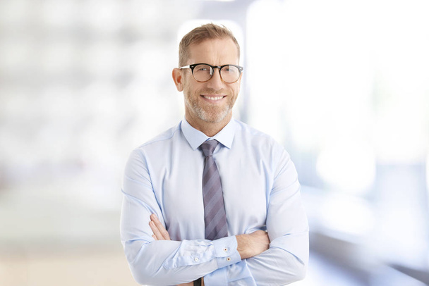 Portrait of middle aged businessman wearing shirt and tie while standing with arms crossed at the office. - Valokuva, kuva