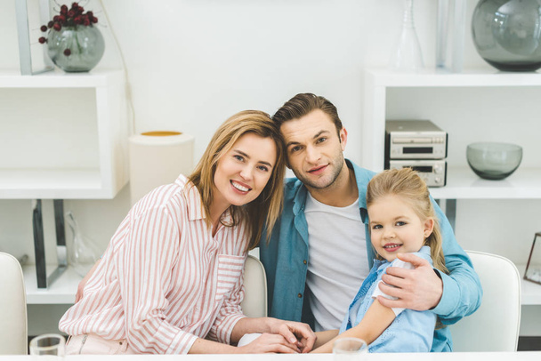 portrait of smiling parents and daughter looking at camera at home - Foto, Imagen