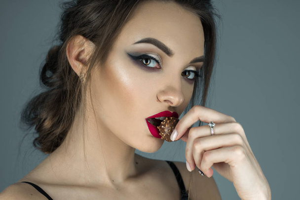 beautiful girl with red lips eats chocolate candy and looking at - Foto, afbeelding