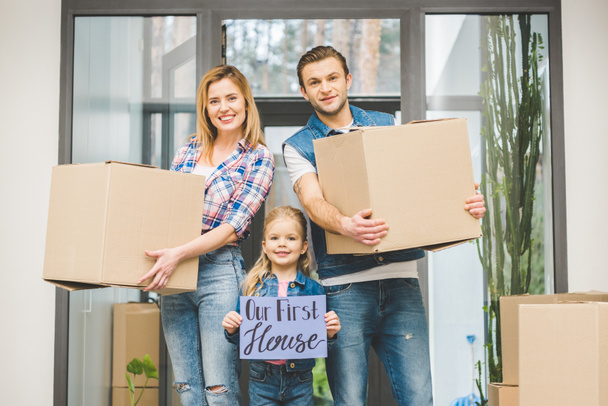portrait of smiling parents and daughter with our new house board in hands, moving home concept - Photo, Image