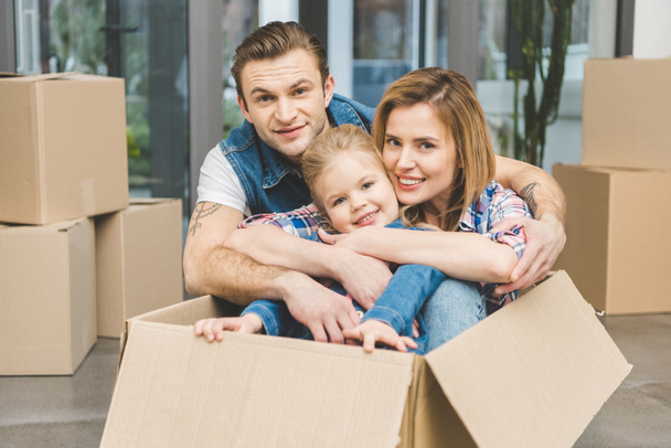 portrait of smiling parents and little daughter in cardboard box at new home, moving home concept - Photo, Image