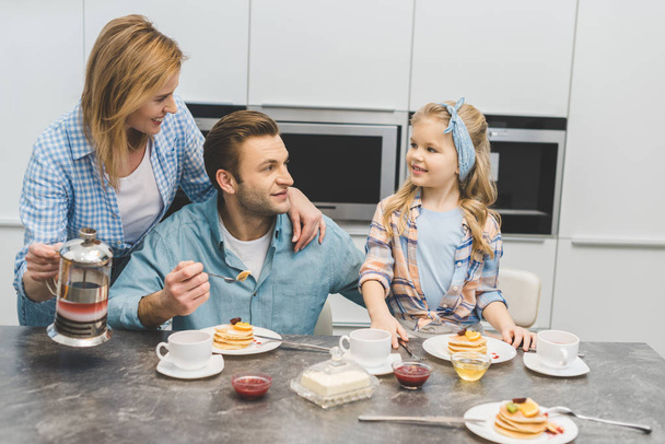 parents and little daughter having breakfast together at home - Foto, afbeelding