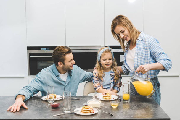 retrato de la mujer vertiendo jugo en el vaso durante el desayuno con la familia en casa
 - Foto, imagen
