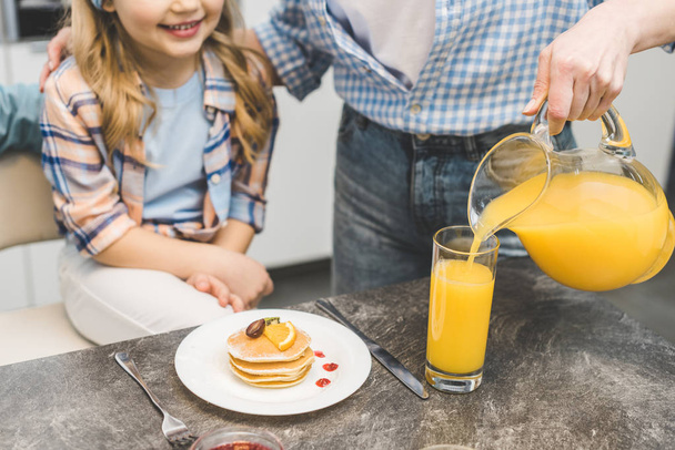 partial view of woman pouring juice into glass during breakfast with daughter - Photo, Image