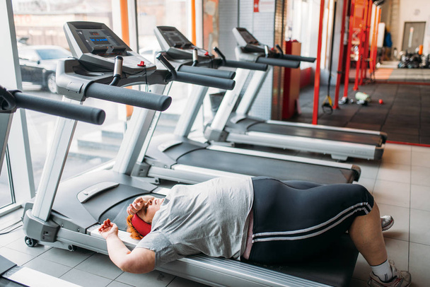 Gruba kobieta zmęczona, leżącego na bieżni, po uruchomieniu w siłowni - Zdjęcie, obraz