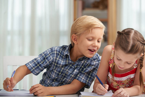 Lachende schooljongen cribbing van papier van zijn klasgenoot - Foto, afbeelding