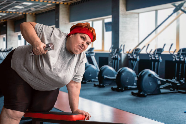 mujer gorda haciendo ejercicio con la mancuerna en el gimnasio
 - Foto, Imagen