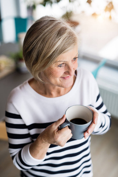 Senior woman holding a cup of coffee in the kitchen. - Foto, Imagem
