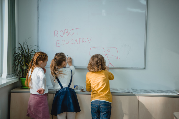 visión trasera de los niños escribiendo y dibujando señales de educación robot en pizarra blanca
 - Foto, Imagen