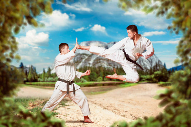 Maîtres de karaté d'arts martiaux en kimono blanc et ceintures noires, entraînement de combat en plein air, coup de pied dans le saut
 - Photo, image
