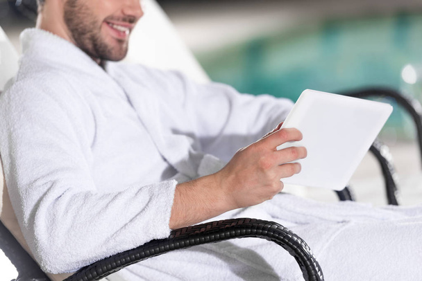 rajattu laukaus hymyilevä mies kylpytakki käyttäen digitaalista tabletti kylpyläkeskuksessa
 - Valokuva, kuva