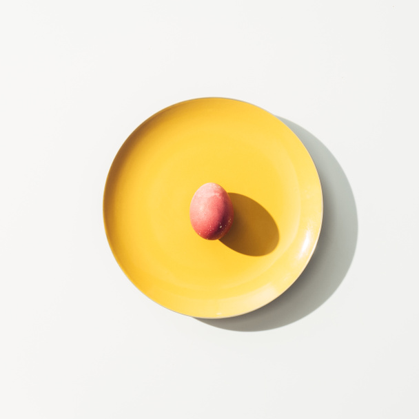 верхний вид красного пасхального яйца на желтую тарелку, на белый
 - Фото, изображение