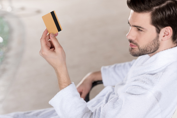 young man in bathrobe holding credit card in spa center   - Photo, Image
