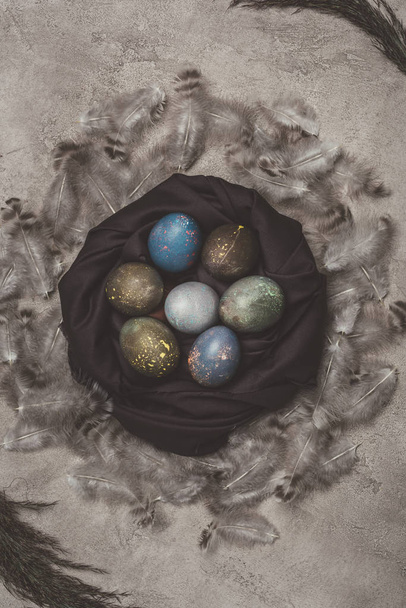top view of easter eggs in nest with feathers on concrete surface - Photo, Image