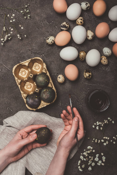 vista ritagliata dell'uomo che dipinge uova di Pasqua e le mette in vassoio, fiori, quaglie e uova di pollo vicino
 - Foto, immagini