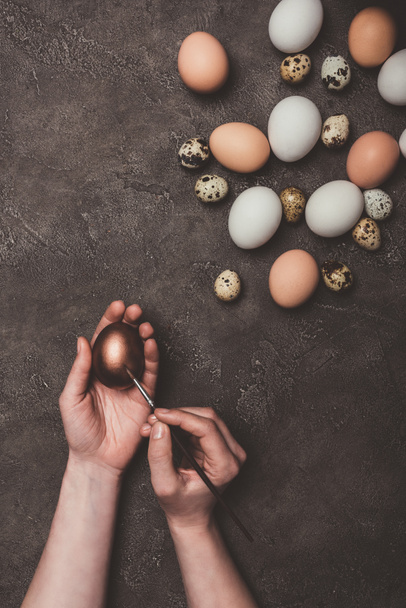 cropped view of man painting golden easter egg, quail and chicken eggs near - Foto, Imagen