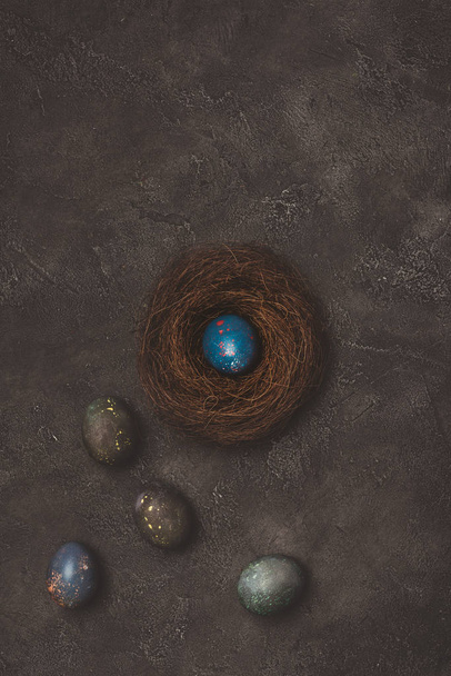 vista superior del huevo de Pascua azul en el nido con huevos pintados cerca de la mesa de hormigón
 - Foto, imagen