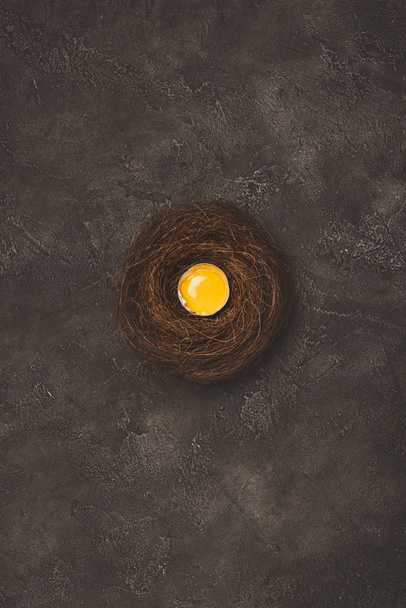 Draufsicht auf zerbrochenes Ei mit Eigelb im Nest auf Betonoberfläche  - Foto, Bild