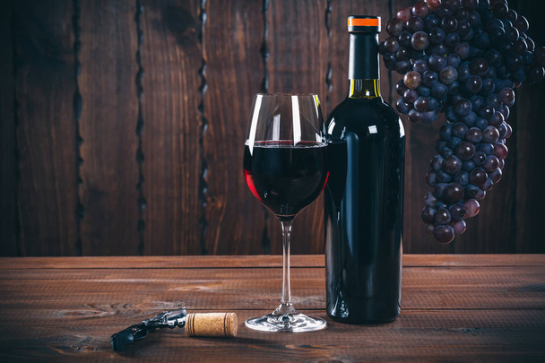 Flasche und Glas Rotwein, Trauben und Kork auf Holzgrund. - Foto, Bild