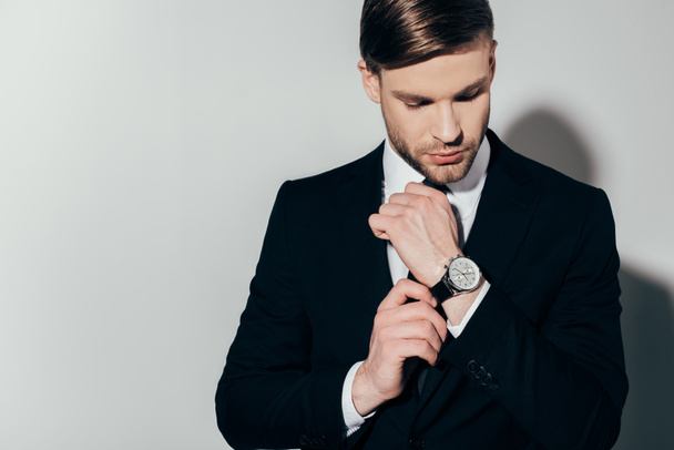 Pensativo empresario confiado en traje de fijación de su reloj sobre fondo blanco
 - Foto, imagen