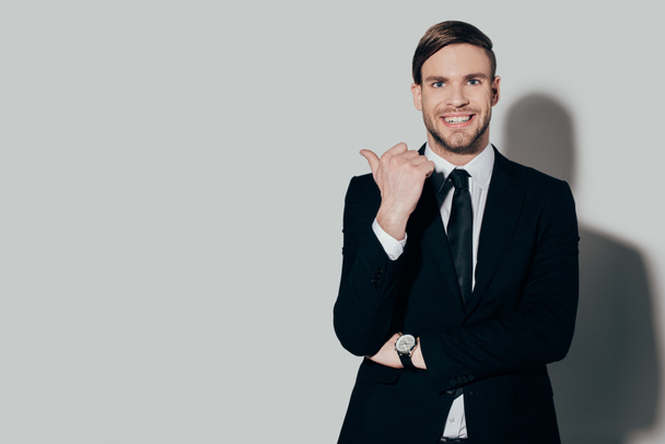 Homem de negócios elegante em terno sorrindo e apontando no fundo branco
 - Foto, Imagem