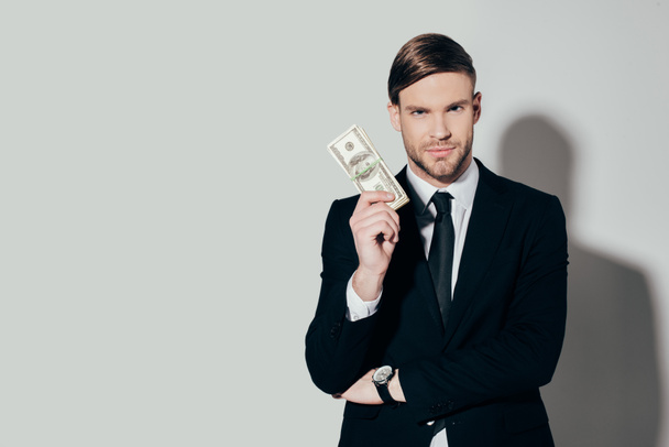 Young confident businessman in suit showing dollar banknote looking at camera on white background - Valokuva, kuva