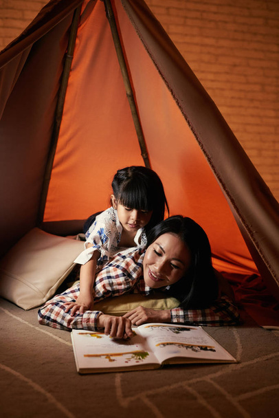母と娘の家と読む絵本でテントの中で横になっています。 - 写真・画像