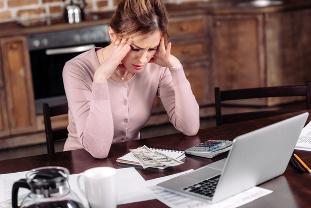 портрет разочарованной женщины, сидящей за столом с деньгами, ноутбуком и бумагами дома, концепция финансовых проблем
 - Фото, изображение