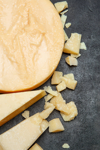 Head of parmesan or parmigiano hard cheese and pieces on concrete background - Photo, Image